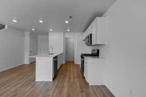 Kitchen with appliances with stainless steel finishes, dark hardwood / wood-style floors, white cabinetry, and sink