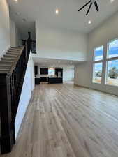 Unfurnished living room featuring ceiling fan, light hardwood / wood-style flooring, and a high ceiling