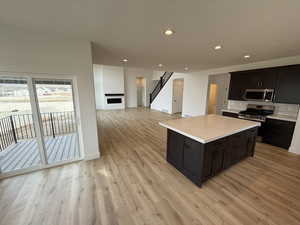 Kitchen featuring a kitchen island, appliances with stainless steel finishes, light wood-type flooring, backsplash, and a textured ceiling