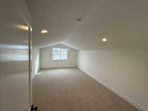 Bonus Room Additional living space featuring light carpet, a textured ceiling, and a lofted ceiling