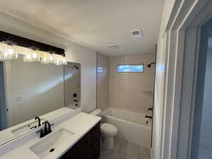 Full bathroom with a textured ceiling, vanity, tiled shower / bath combo, and toilet