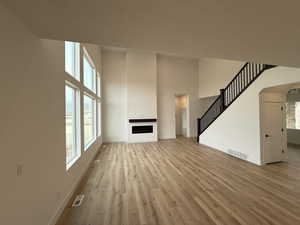 Unfurnished living room with a high ceiling, a textured ceiling, and light wood-type flooring