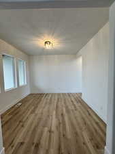 Empty room with light hardwood / wood-style floors and a textured ceiling