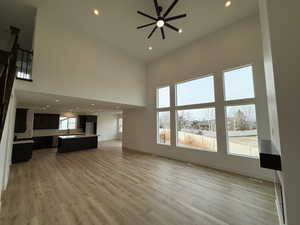 Unfurnished living room featuring ceiling fan, a towering ceiling, sink, and light wood-type flooring