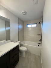 Full bathroom with vanity, a textured ceiling, tiled shower / bath combo, and toilet