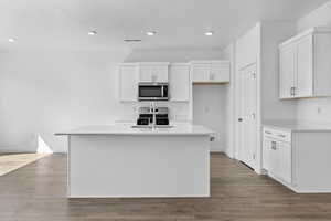 Kitchen featuring sink, stainless steel appliances, an island with sink, wood-type flooring, and white cabinets