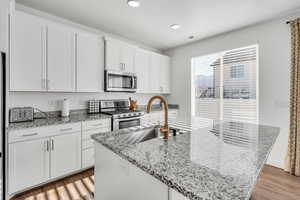 Kitchen featuring light stone counters, stainless steel appliances, a kitchen island with sink, sink, and white cabinets