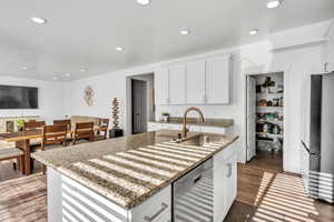 Kitchen featuring appliances with stainless steel finishes, light stone counters, a kitchen island with sink, sink, and white cabinets