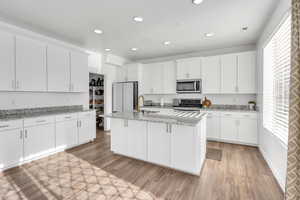 Kitchen featuring appliances with stainless steel finishes, white cabinetry, and light stone counters