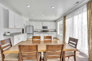 Kitchen with a kitchen island with sink, light wood-type flooring, light stone countertops, appliances with stainless steel finishes, and white cabinetry