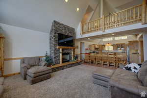 Carpeted living room featuring high vaulted ceiling and a stone fireplace