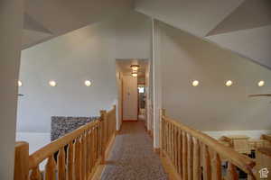 Corridor featuring light carpet and vaulted ceiling.