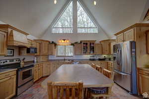 Kitchen featuring custom exhaust hood, high vaulted ceiling, sink, light brown cabinetry, and stainless steel appliances