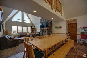 Dining space featuring tile patterned flooring, a stone fireplace, and high vaulted ceiling