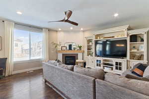 Living room with a textured ceiling, dark hardwood / wood-style flooring, a brick fireplace, and ceiling fan