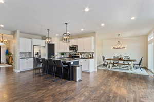 Kitchen featuring a center island with sink, a kitchen breakfast bar, white cabinets, decorative light fixtures, and stainless steel appliances