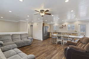 Living room featuring a textured ceiling, ceiling fan, ornamental molding, and dark wood-type flooring