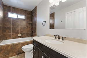 Full bathroom with vanity, tiled shower / bath, tile patterned flooring, toilet, and a textured ceiling