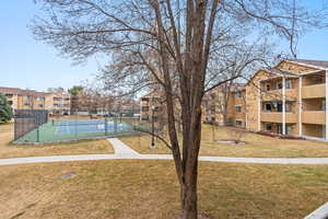 View of home's community with tennis court and a lawn