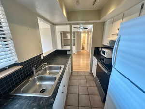 Kitchen featuring white appliances, white cabinets, dark tile patterned flooring, sink, and tasteful backsplash