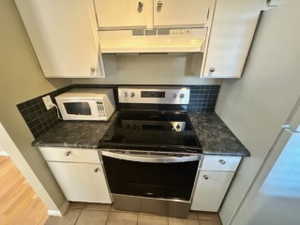 Kitchen featuring backsplash, dark stone counters, white appliances, light tile patterned floors, and white cabinetry