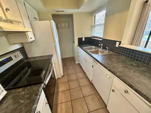 Kitchen with white cabinets, a raised ceiling, sink, stainless steel electric range oven, and light tile patterned floors