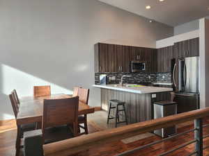 Kitchen with dark brown cabinetry, a high ceiling, kitchen peninsula, a kitchen bar, and appliances with stainless steel finishes