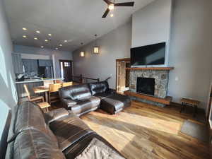 Living room featuring a stone fireplace, ceiling fan, wood flooring, and lofted ceiling