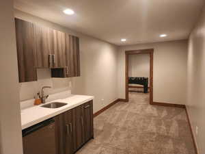 Wet bar with stainless beverage fridge, sink, dark brown cabinetry, and light carpet