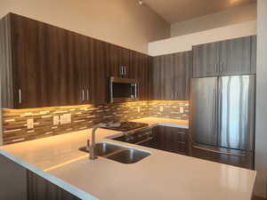 Kitchen featuring kitchen peninsula, tasteful backsplash, dark brown cabinets, stainless steel appliances, Thermador stove