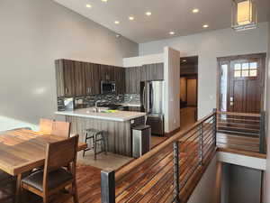 Kitchen featuring backsplash, kitchen peninsula, appliances with stainless steel finishes, dark brown cabinetry, and a breakfast bar area