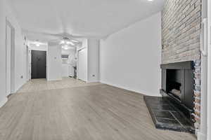 Unfurnished living room featuring ceiling fan, a brick fireplace, and light hardwood / wood-style flooring