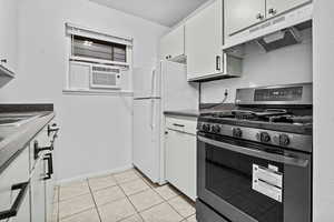 Kitchen featuring light tile patterned flooring, stainless steel gas stove, cooling unit, white cabinets, and white fridge