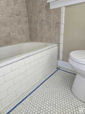 Bathroom featuring tile patterned floors, tiled bath, and toilet