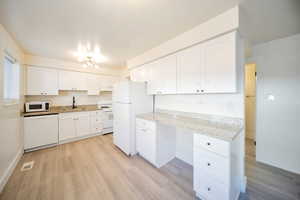 Kitchen with white cabinets, white appliances, light hardwood / wood-style floors, and sink