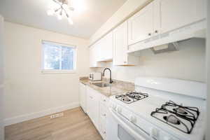 Kitchen with light stone countertops, white appliances, sink, light hardwood / wood-style floors, and white cabinetry