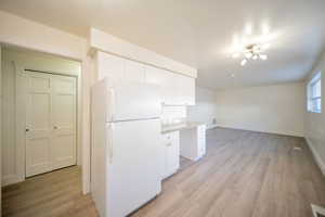 Kitchen with white cabinets, light wood-type flooring, white refrigerator, and light stone countertops