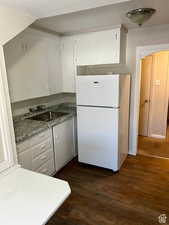 Kitchen featuring white refrigerator, white cabinetry, dark wood-type flooring, and sink