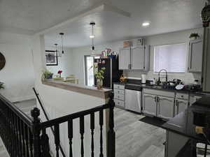 Kitchen featuring dishwasher, black fridge, light hardwood / wood-style floors, decorative light fixtures, and decorative backsplash