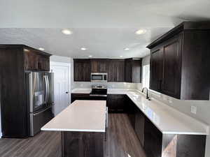 Kitchen with sink, stainless steel appliances, dark hardwood / wood-style flooring, dark brown cabinets, and a kitchen island