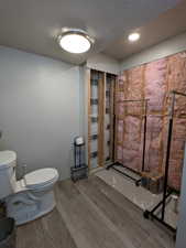 Partially finished bathroom with toilet, wood-type flooring, and a textured ceiling