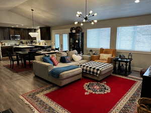 Living room with wood-type flooring, lofted ceiling, and a notable chandelier