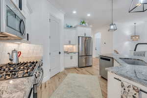 Kitchen with light stone counters, stainless steel appliances, sink, decorative light fixtures, and white cabinetry