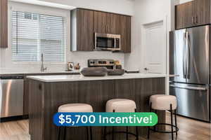 Kitchen with dark brown cabinets, a kitchen breakfast bar, stainless steel appliances, light hardwood / wood-style floors, and a center island