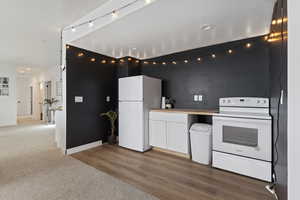 Kitchen featuring carpet, white appliances, and white cabinetry