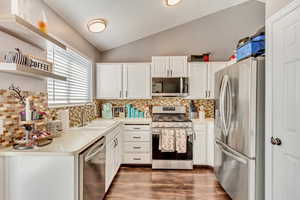 Kitchen with white cabinets, decorative backsplash, stainless steel appliances, and lofted ceiling