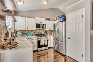 Kitchen with lofted ceiling, sink, tasteful backsplash, white cabinetry, and stainless steel appliances