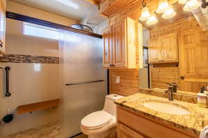 Bathroom with vanity, toilet, a shower with door, and wooden walls