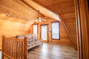 Unfurnished bedroom with light wood-type flooring, rail lighting, rustic walls, wood ceiling, and lofted ceiling