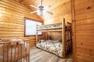 Bedroom featuring rustic walls, ceiling fan, high vaulted ceiling, wooden ceiling, and hardwood / wood-style floors